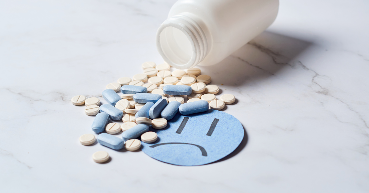 Spilled pills beside a sad face cutout, representing the link between antidepressants and insomnia | Sip2Sleep®