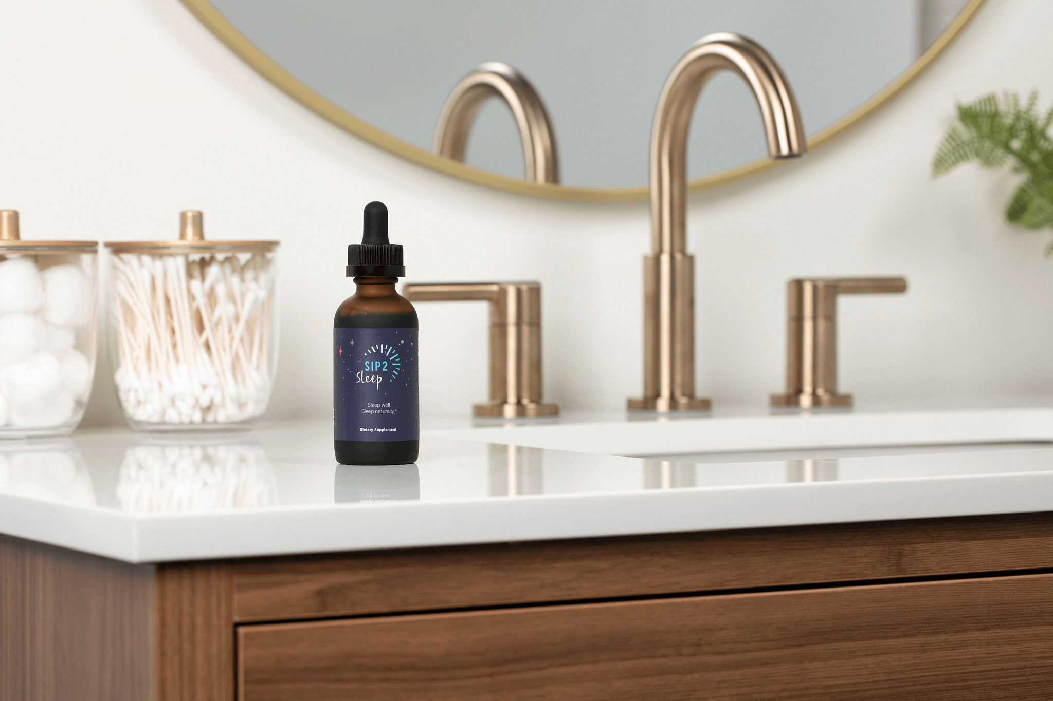 A dark glass bottle labeled "SIP2 Sleep" sits on a modern bathroom countertop beside cotton and swabs, with sleek gold faucets in the background