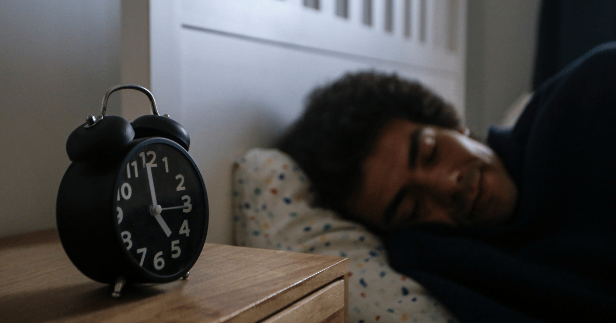 Man sleeping next to bedside alarm clock at night