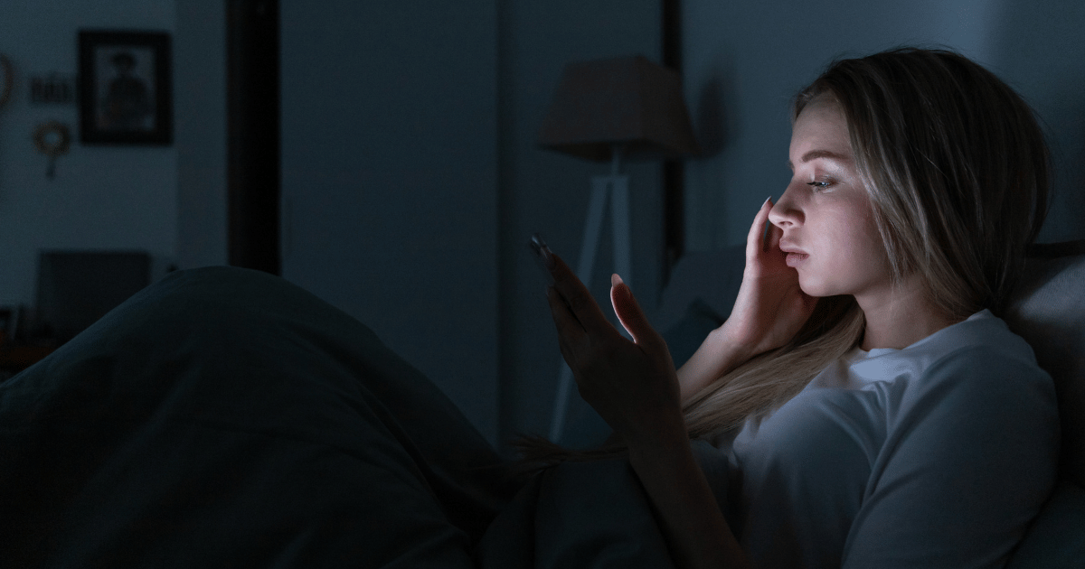 Woman scrolling on phone in bed at night before sleep