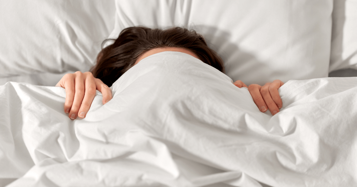Woman lying in bed with blanket pulled up to her nose, adjusting to a new sleep environment | Sip2Sleep®