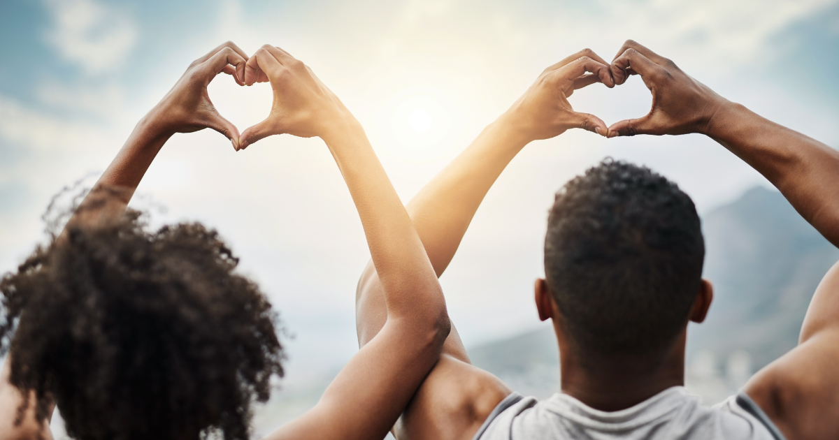 Two people forming heart shapes with their hands, symbolizing heart health and wellness in natural sunlight.