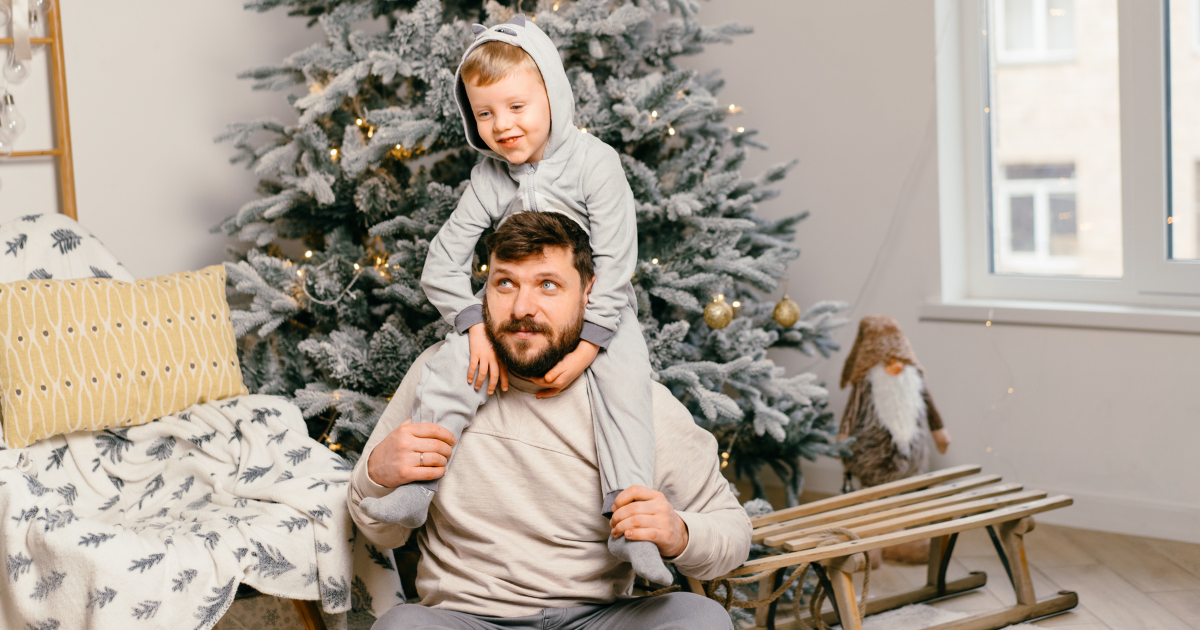 Father and child relaxing by a Christmas tree, symbolizing stress relief and better sleep during the holidays