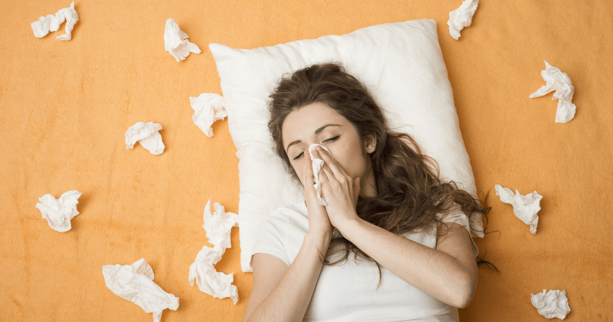 Sick woman lying in bed surrounded by tissues, illustrating the link between inflammation and sleep loss | Sip2Sleep®