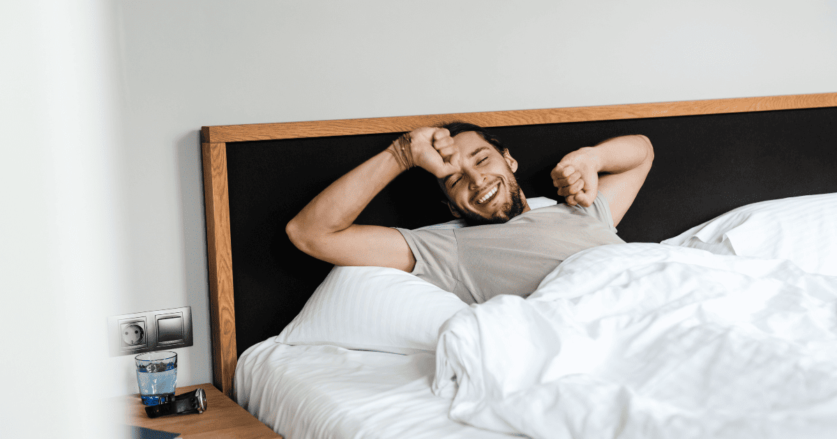 Man waking up in bed, stretching and smiling in the morning.