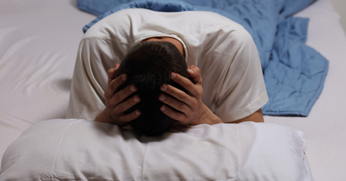 Man in bed with his head in his hands, illustrating the stress and frustration of chronic sleep deprivation