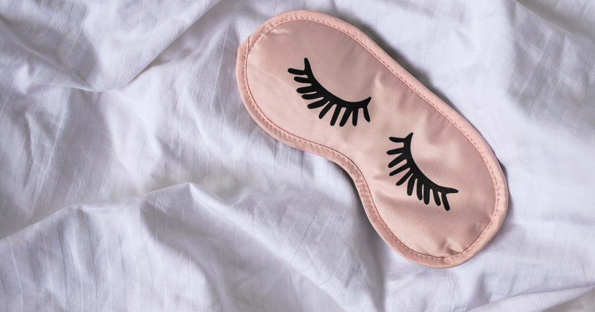 Closed sleeping eye mask with eyelash design on white bed sheets