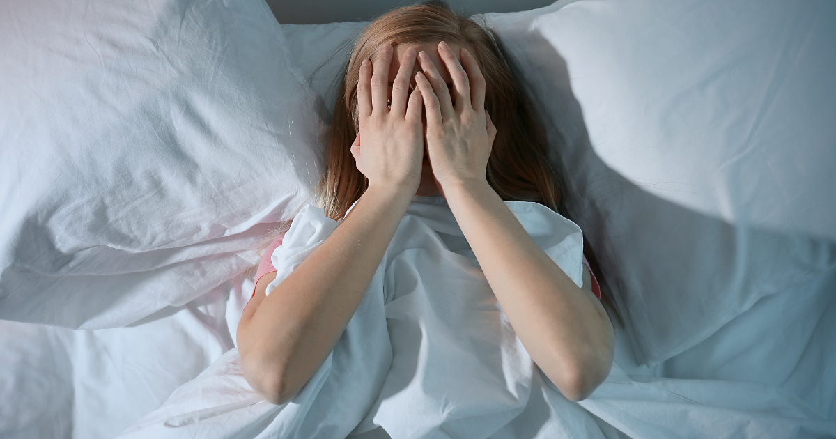 Woman lying in bed with hands covering her face, unable to move during sleep paralysis | Sip2Sleep®
