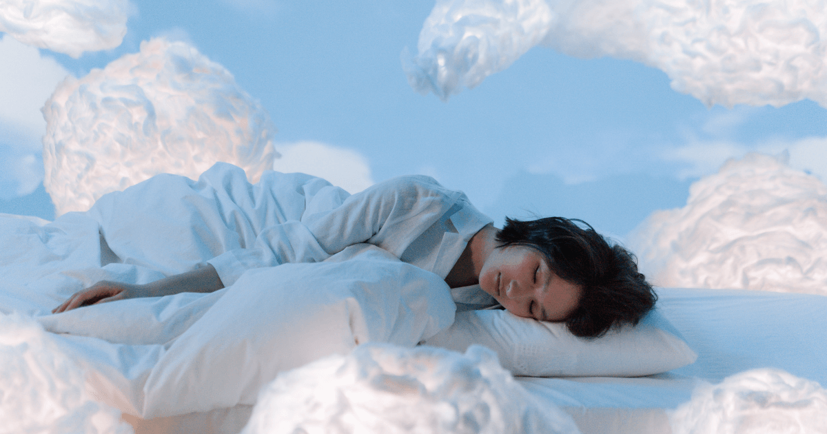Woman sleeping peacefully on a bed with cloud-like surroundings and a soft blue background | Sip2Sleep®