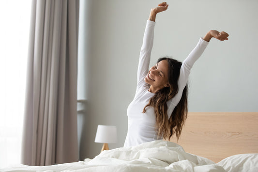 Woman stretching happily in bed after waking up, demonstrating the benefits of natural sleep alternatives for a refreshing morning