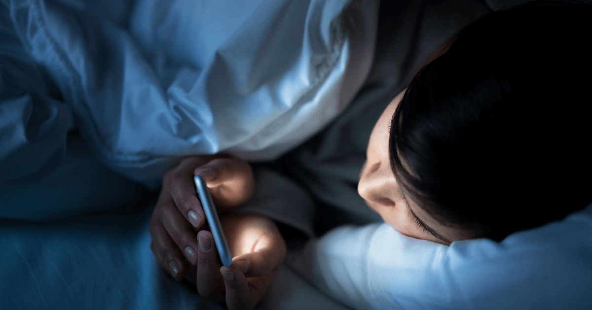 Women using her phone under the blanket in bed at night