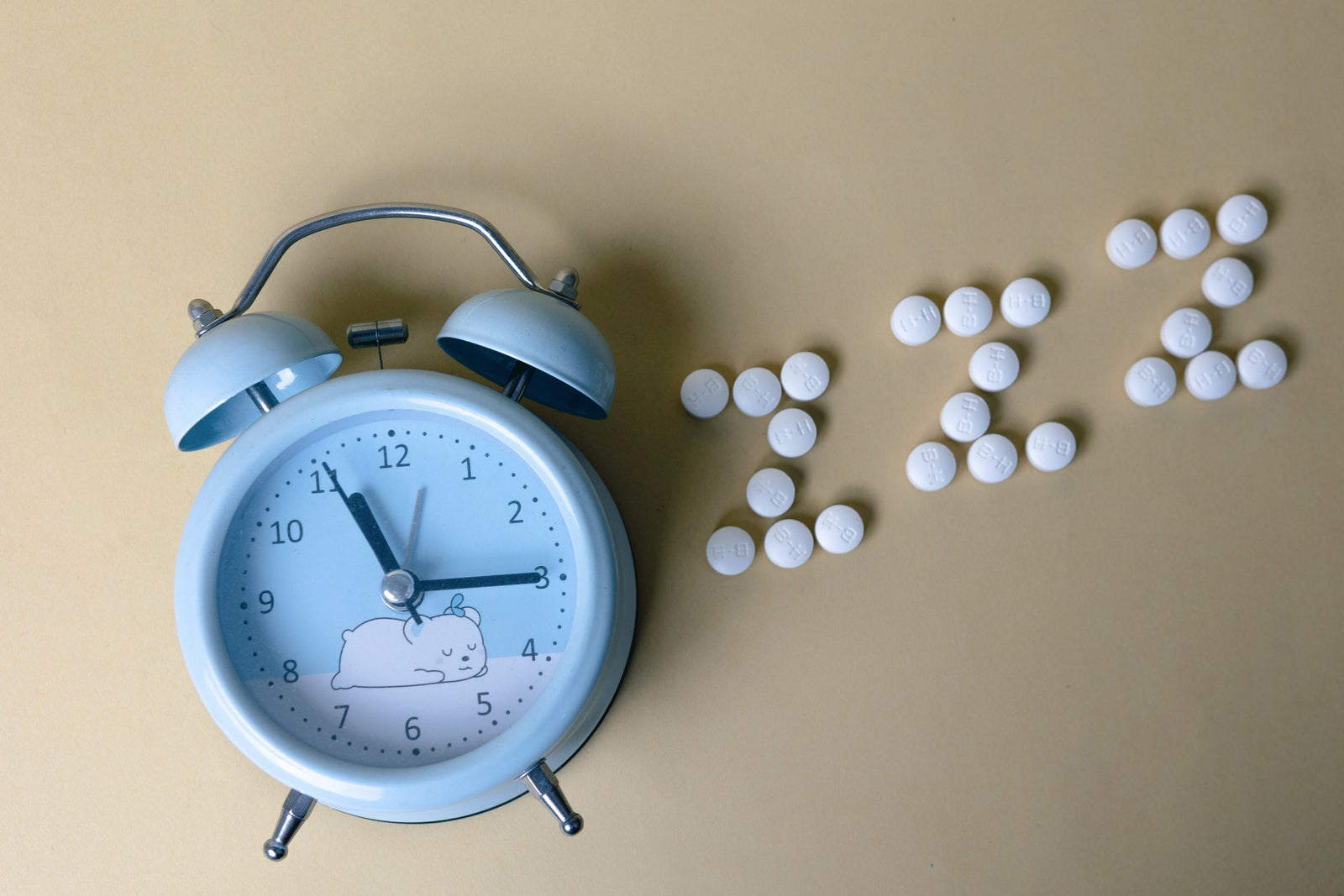 Alarm clock with sleep pills arranged in ZZZ pattern, illustrating melatonin supplements and sleep aid safety concerns | Sip2Sleep®