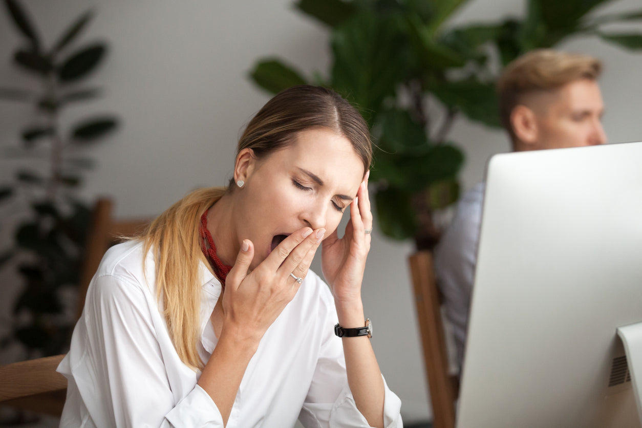 A tired and exhausted woman yawns at her desk, illustrating the negative impact of sleep deprivation on productivity and well-being.